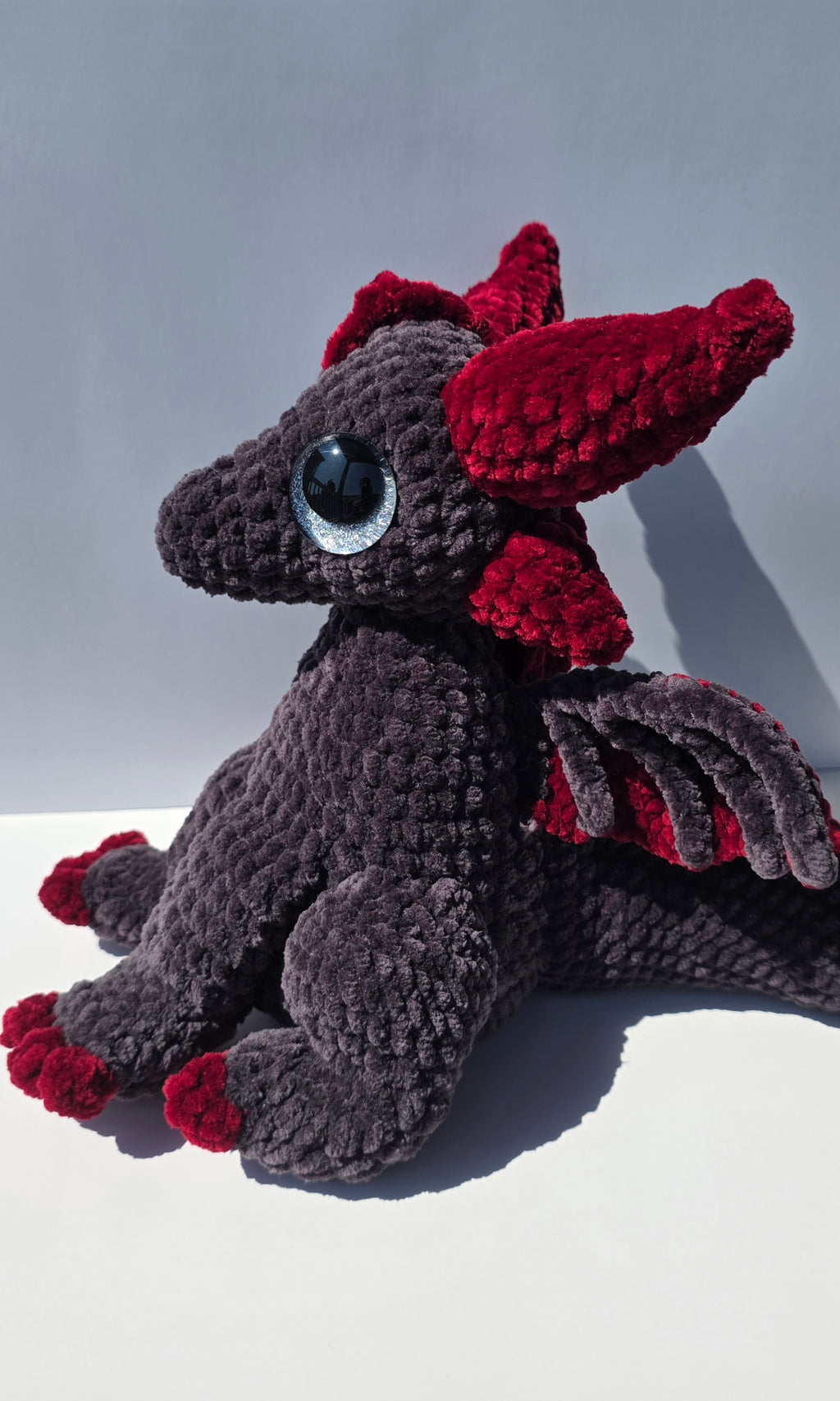 Peluche de dragón sentado con ojos brillantes de colores