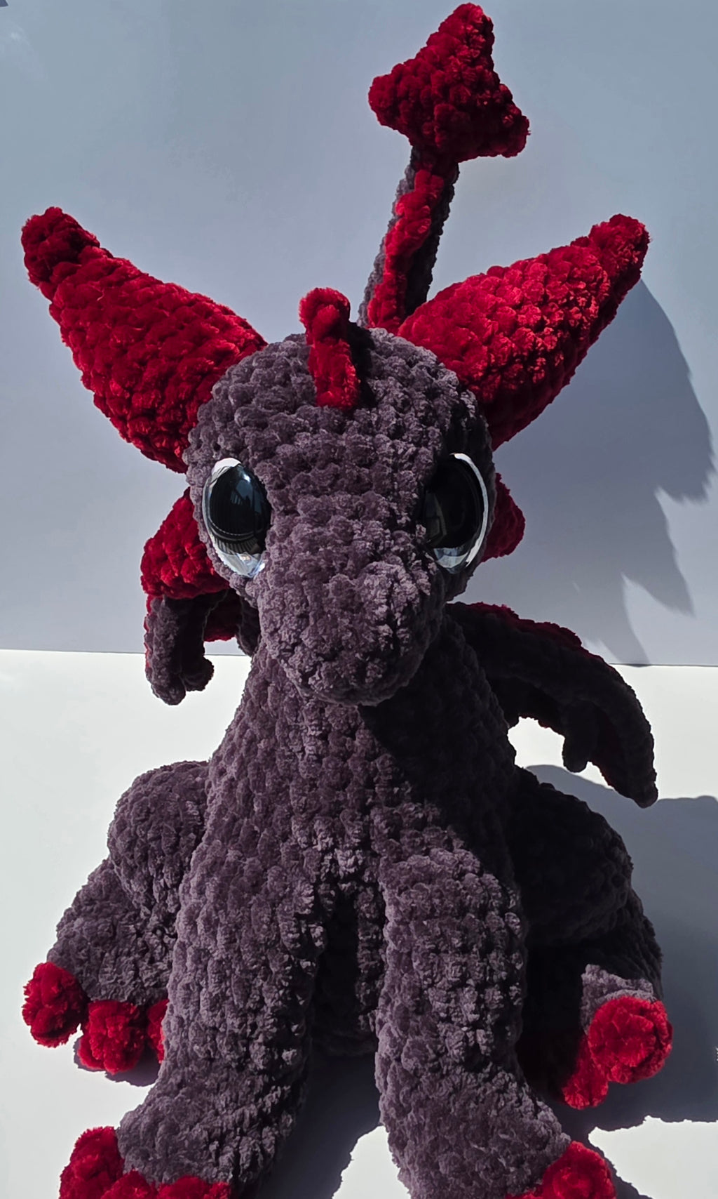 Peluche de dragón sentado con ojos brillantes de colores