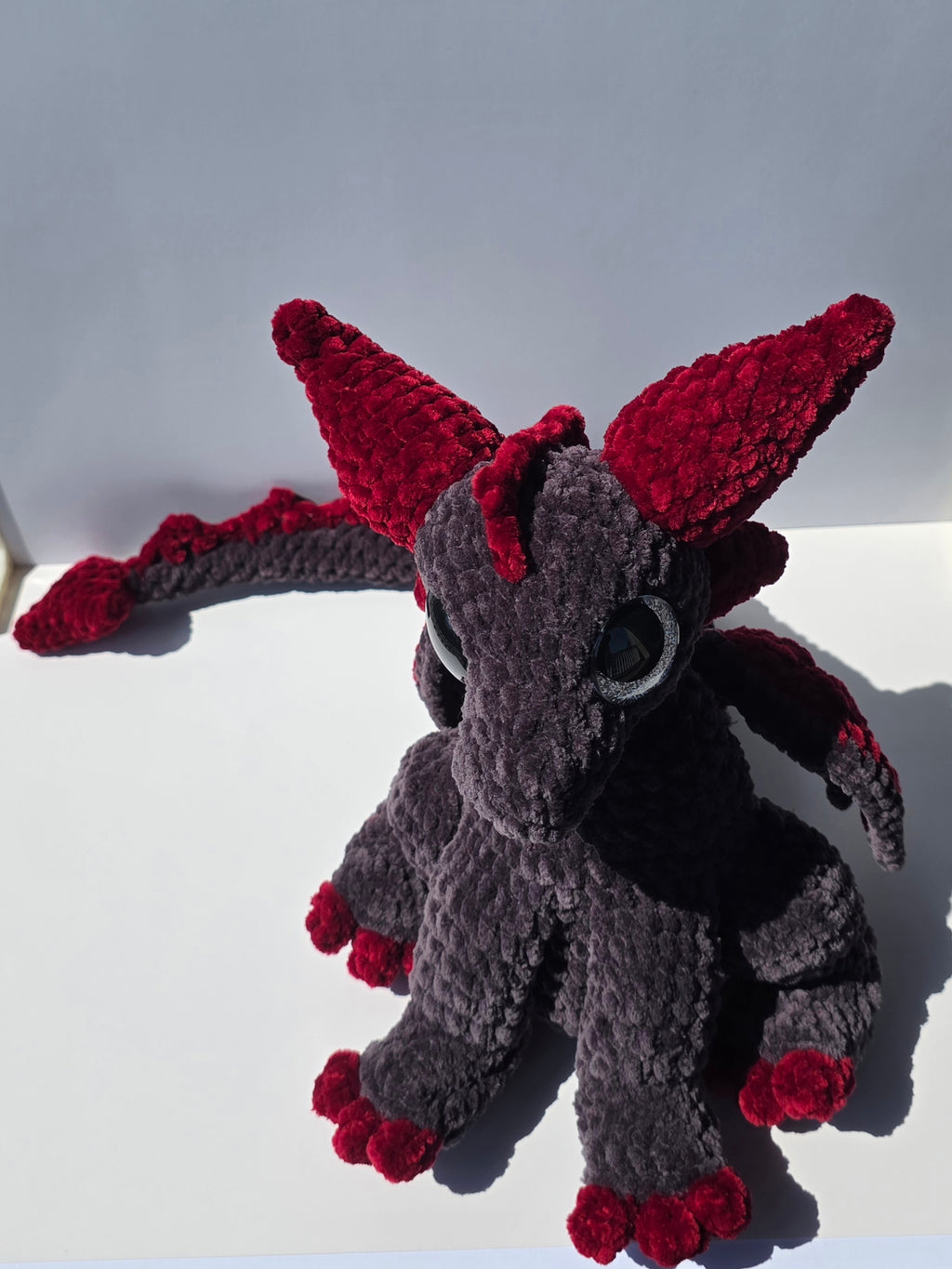 Peluche de dragón sentado con ojos brillantes de colores